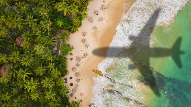 Airplane silhouette over a tropical beach with palm trees. Travel and resort vacation concept 