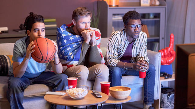 Friends watching football match at home lit by blue light 