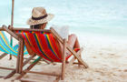 View from behind of a woman reading while sitting on beach 