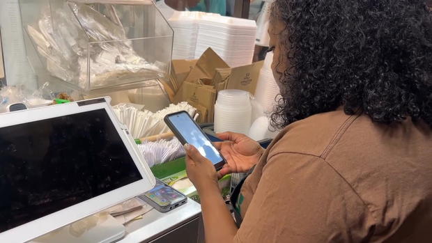 Careda Matthews looks at her phone while behind the counter at her food stand at Reading Terminal Market 