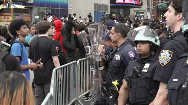 NYPD officers stand on the other side of barriers as a crowd. 