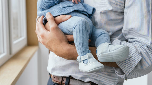 Cropped close-up of father holding baby by window at home 