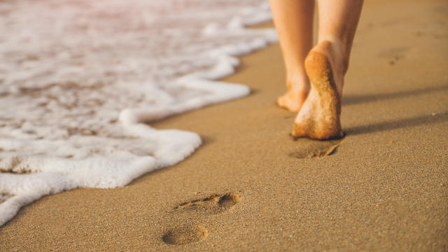 Woman walking on sand beach leaving footprints in the sand 