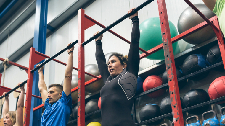 Three people prepare to do pull-ups alongside each other in a gym.