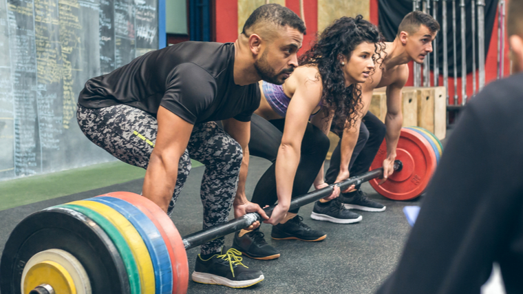 Three people prepare to lift the same, long, heavy loaded barbell.