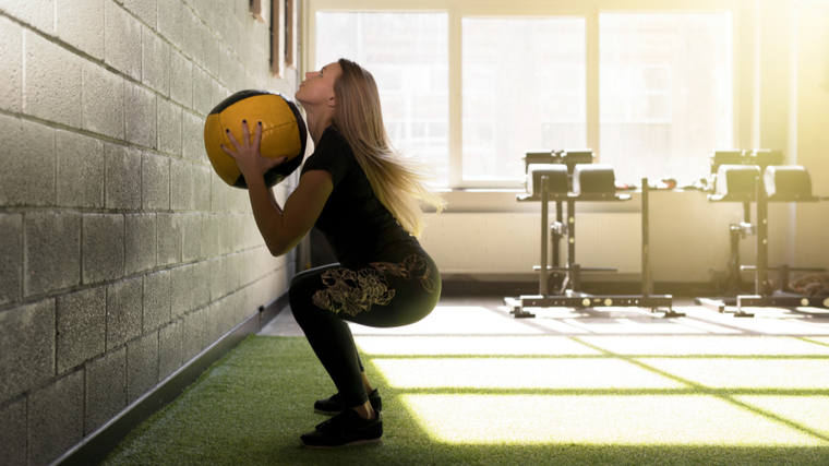 A person with long hair squats down before performing a wall ball.