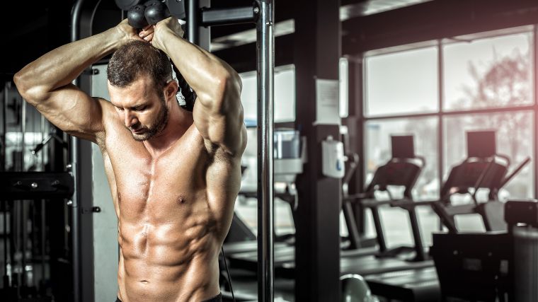 A shirtless bodybuilder performing an overhead triceps extension.