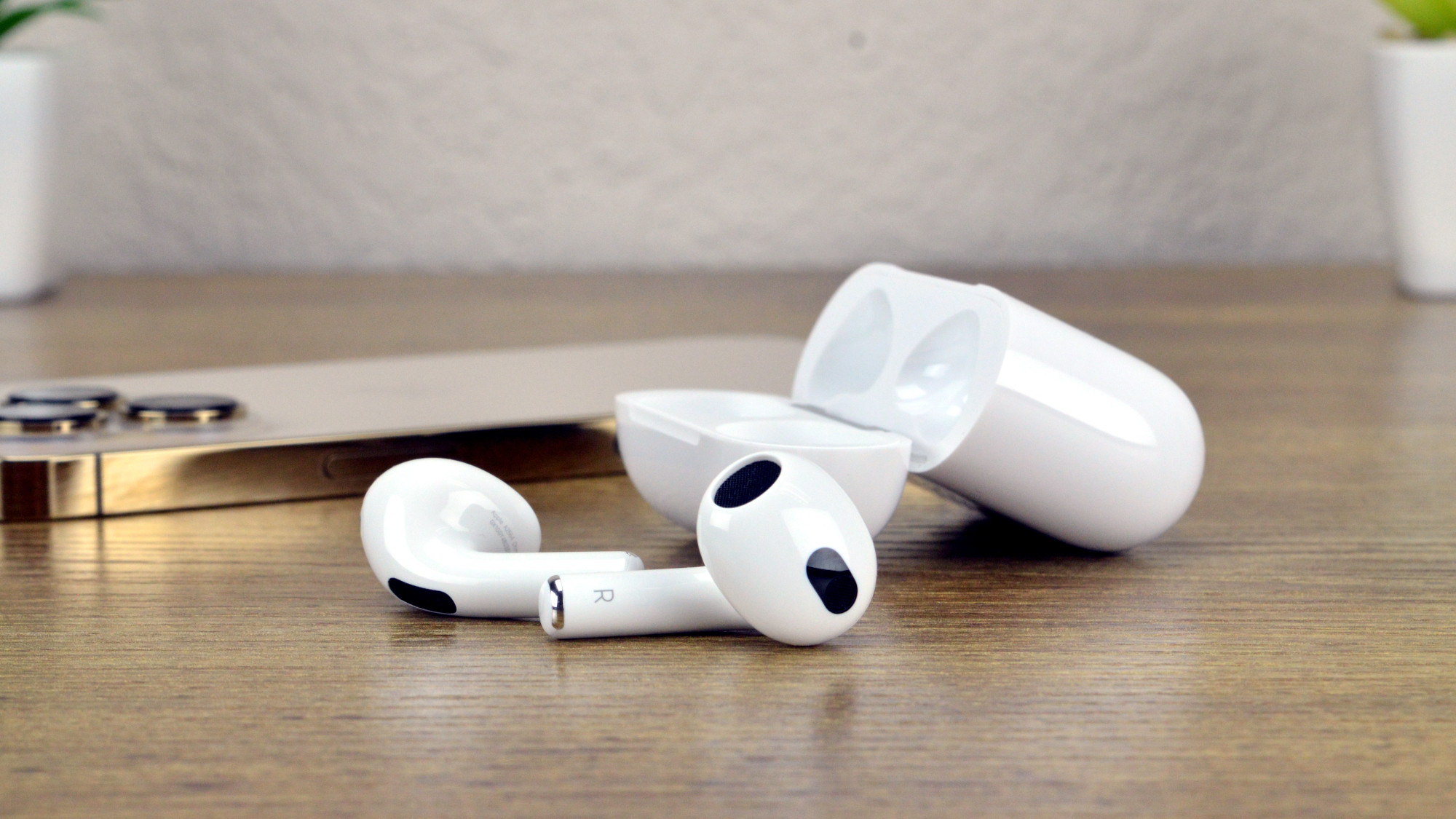 Apple AirPods 3 on a table next to an iPhone 13 Pro