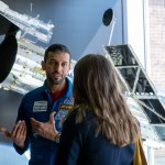 NASA intern Julia Tilton interviews UAE astronaut Sultan al-Neyadi. al-Neyadi wears the iconic blue jumpsuit of an astronaut and gestures with his hands. Tilton is facing away from the camera and speaks with al-Neyadi in business professional attire. Credit: NASA