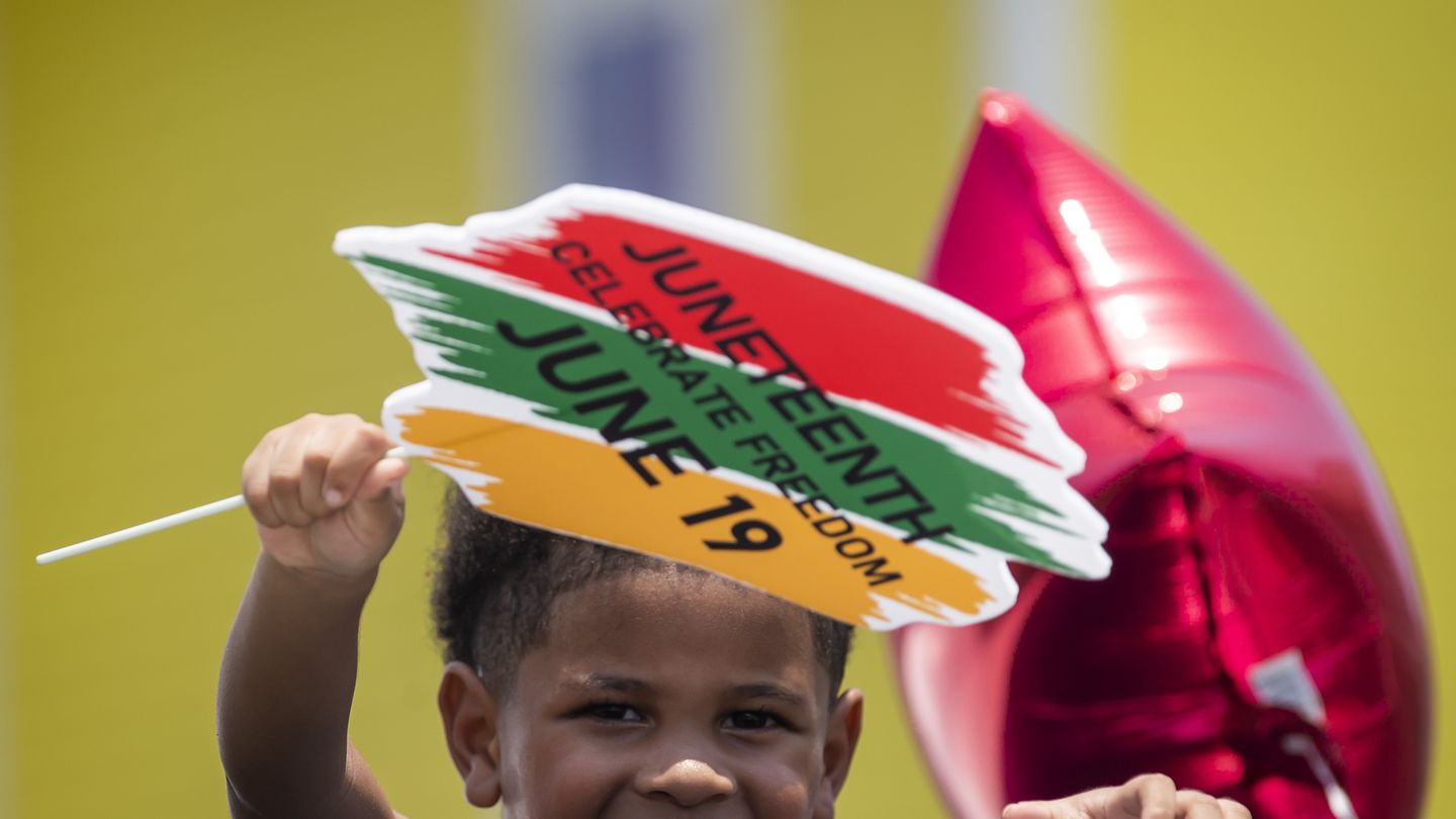 Kici Ashton, 3, waves a Juneteenth sign from a car while riding in the annual Galveston Juneteenth Parade in Galveston, Texas, in 2023.