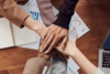 Six arms extended holding hands in the centre of a work table