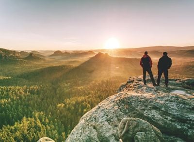 Two hikers standing on top of summit above valley 