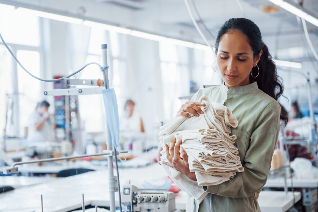 Photo: Woman dressmaker stands in the factory with cloth in hands.