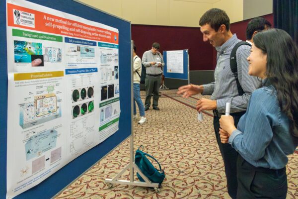 Prof. Rumyantsev and a woman talk in front of a research poster