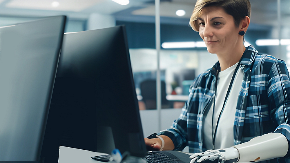 A woman with a prosthetic arm working intently on a computer in a modern office environment.