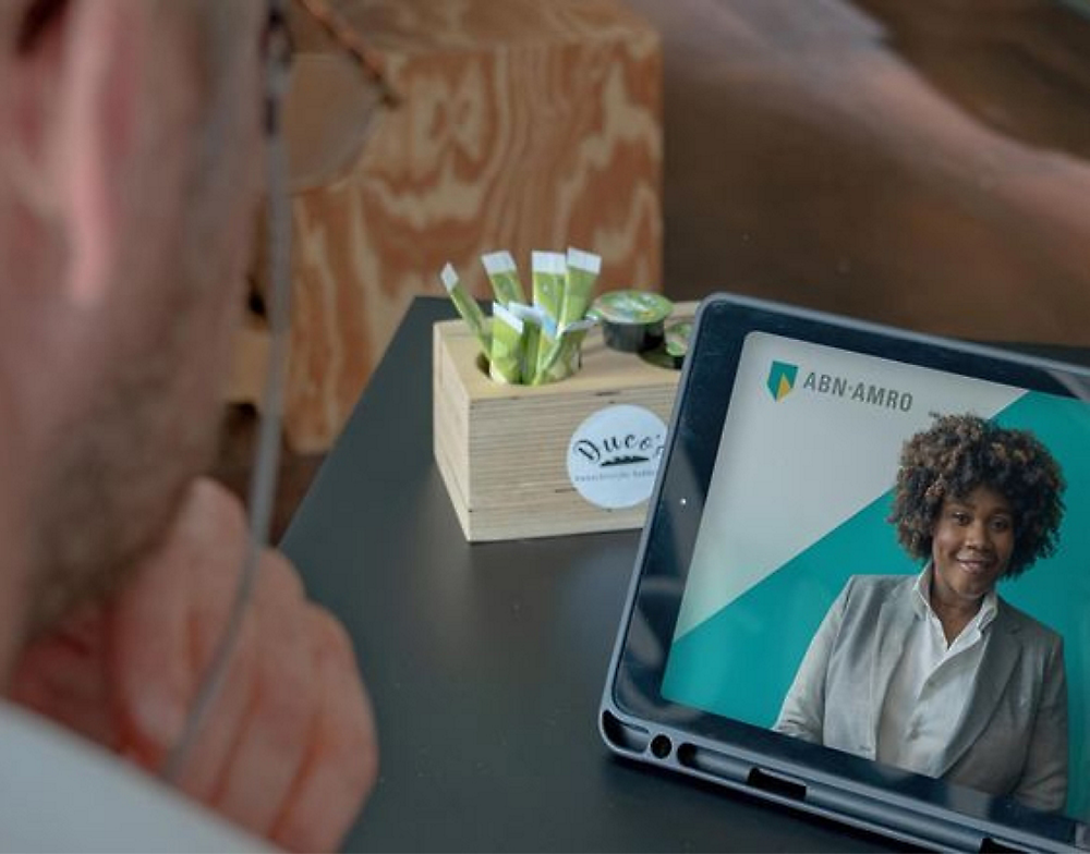 A person watching a business presentation on a tablet featuring a female speaker from abn-amro.