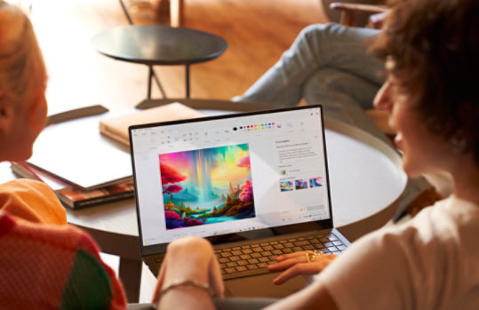 Zwei Personen sitzen vor einem Laptop mit geöffneter Paint-App