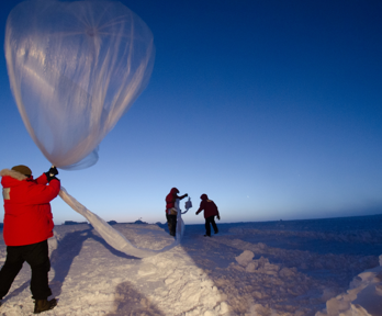 Three people undertake nondescript research in a seemingly artic environment. The snowy landscape stretches as far as the eyes can see