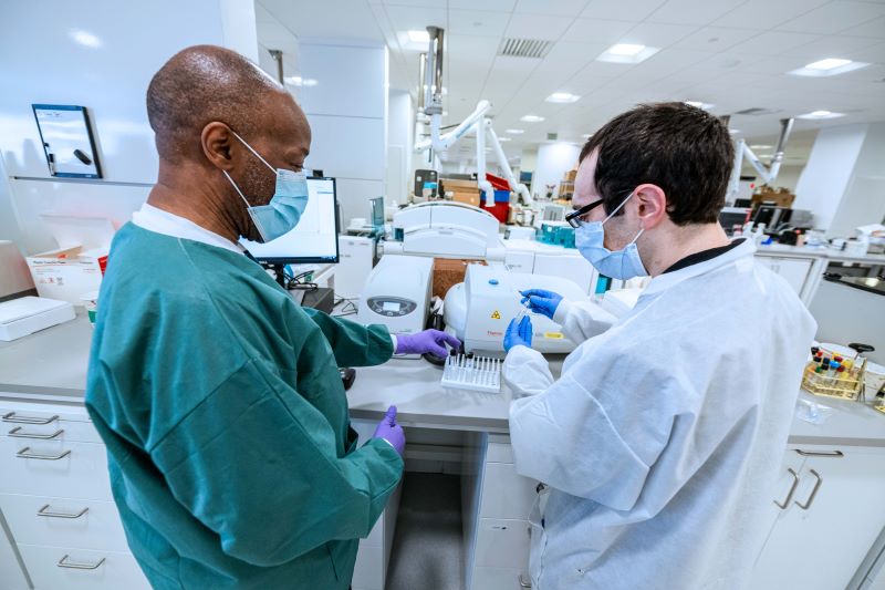 2 laboratory professionals wearing masks and working with vials.