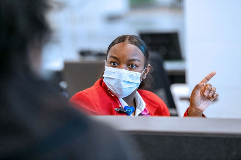 Masked woman at a desk, pointing in a direction for a visitor