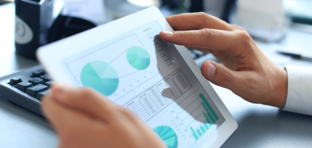 Close-up of a person’s hands holding a computer tablet and touching the screen that shows graphs and pie charts