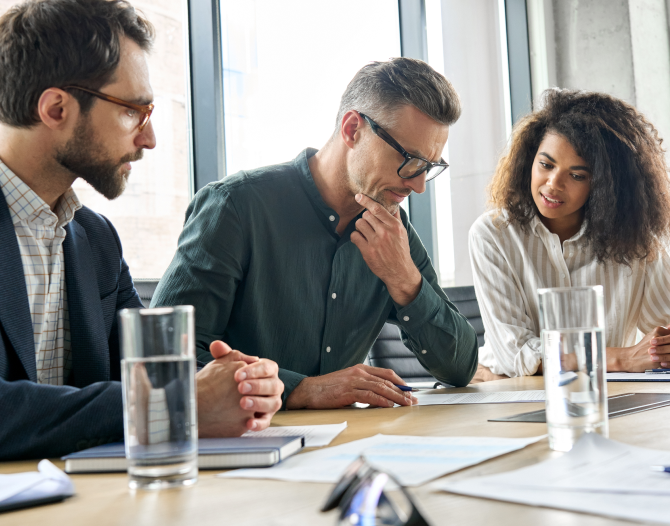 Three business colleagues sitting at a conference room table studying a document.