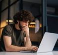 A young man sitting at his kitchen table while working on his laptop.