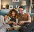 A couple eats popcorn as they watch a show from their couch.