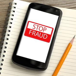 cellphone on top of notebook with yellow pencil on the side, on the screen in red and white &quot;stop fraud&quot; 