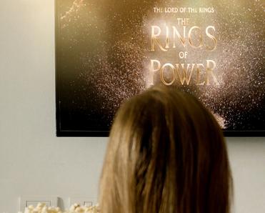 back of the head of a woman having popcorn watching The Lord of The Rings on TV