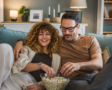 A couple eats popcorn as they watch a show from their couch.