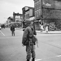 A soldier standing guard in a Washington, D.C. street with the ruins of buildings that were destroyed during the riots that followed the assassination of Martin Luther King, Jr., April 8, 1968.