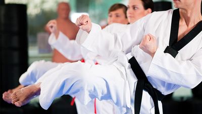 People in a gym in martial arts training exercising Taekwondo, the trainer has a black belt.