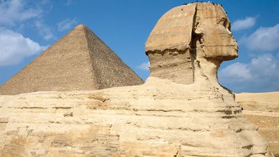 Al-Jizah. Giza Necropolis, Giza Plateau, Cairo, Egypt. Side view of Sphinx with the Great Pyramid of Khufu (Cheops) rising in the background. The sides of all three of the Giza pyramids are astronomically oriented to be north-south, east-west (see notes)