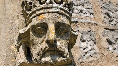 Weathered stone sculpture of a king's head on the side of a Church in Somerset, England. English royalty