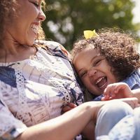 Mother tickling her daughter, sitting in a garden