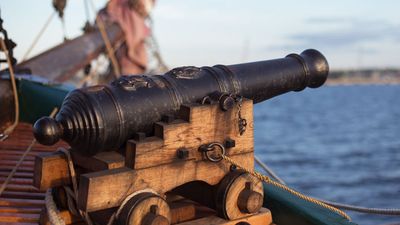 Old medieval wooden pirate military war ship with a cannon on the deck pointed out and aiming