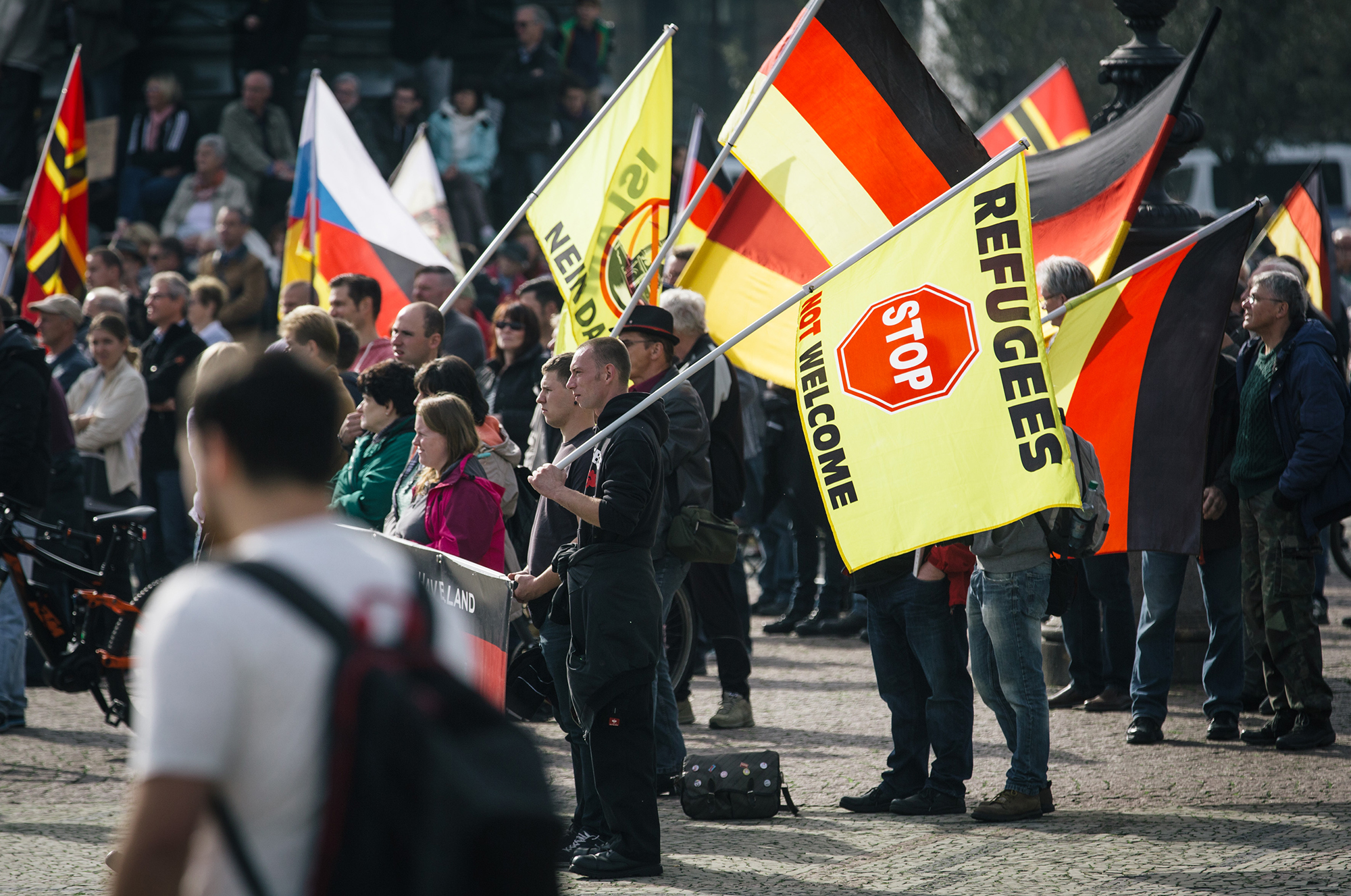 Supporters of the anti-immigrant Pegida movement protest and hold German flags and a sign that reads "STOP Refugees not welcome".