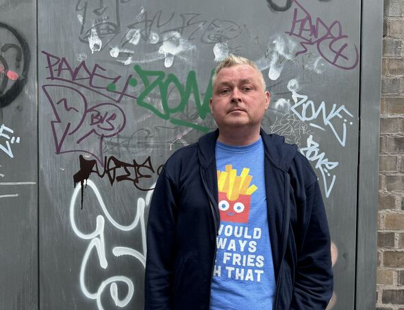 A man in a blue tshirt in front of a grey wall
