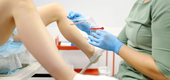 Gynecologist examines a patient laying on gynecological chair using medical vaginal speculum. Doctor takes a smear from a young woman cervix. Diagnosi