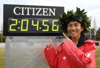 Kengo Suzuki smiles for photos next to the time board showing his record in the 76th Lake Biwa Mainichi Marathon, at Ojiyama Stadium in Otsu, on Feb. 28, 2021. (Mainichi/Rei Kubo)