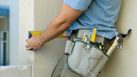 Handwerker mit Werkzeuggürtel legt einen Messwinkel an eine Fensterleibung an