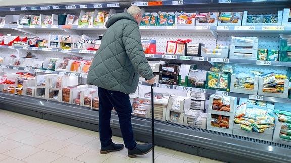 Ein alter Mann steht im Supermarkt vor einem Kühlregal