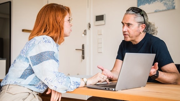 Ein Mann und eine Frau sitzen mit einem Aktenordner und einem Laptop an einem Esstisch.