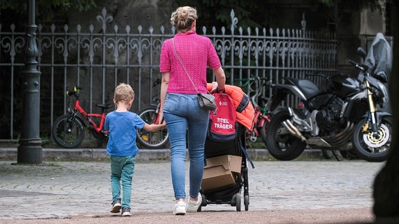 Eine Mutter hält ein Kind an der Hand und schiebt einen Kinderwagen.