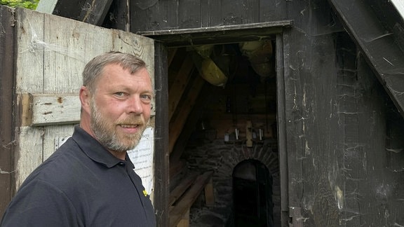 Ein Mann steht vor der geöffneten Eingangstür eines Bergwerkstollens