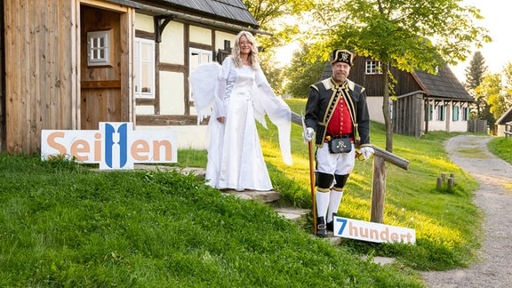 Zwei Menschen als Engel und Bergmann verkleidet stehen auf einer Treppe vor einem Haus