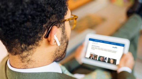 Junger Mann mit In-ear Kopfhörern schaut auf sein Tablet.