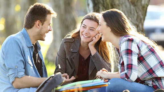 Ein junger Mann und zwei junge Frauen sitzen im Park und lachen