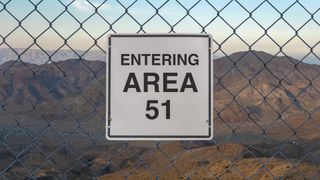 Area 51 sign on fence in the Nevada Desert. The white square sign has the text "entering area 51" written in large black letters.